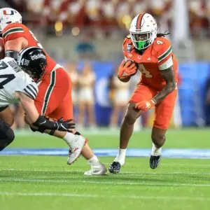 "Miami Hurricanes running back in action during a college football game, evading a tackle."
