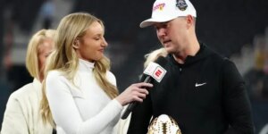 "Sports journalist interviewing a football coach at a post-game event, both dressed in casual attire."