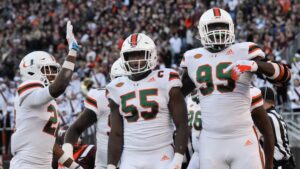 "Miami Hurricanes football players celebrating a win on the field, with number 55 gesturing a victory sign."