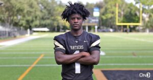 "Panthers football player in full uniform poses confidently on the field with arms crossed"