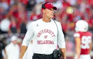 "University of Oklahoma coach during a football game, overseeing players on the field in official team attire"