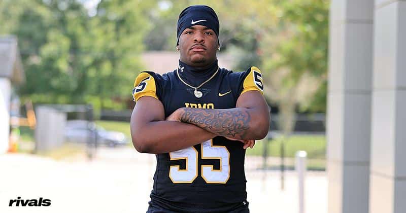 High school football player in Trojan jersey standing with arms crossed at outdoor setting